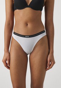 Hvit bikini-truse laget av et mykt materiale, med en svart elastisk midje med "BOSS"-logo. Enkel design med minimal dekning.