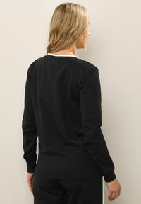 Sudadera negra de manga larga con cuello redondo y puños de canalé. Textura suave, diseño ajustado y estilo minimalista sin adornos.
