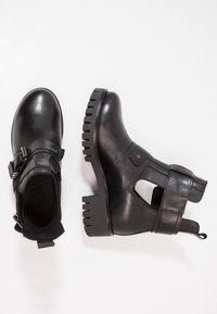 Černé kožené kotníkové boty s robustní podrážkou, detailní sponou a vyřezávanými akcenty. Hladký povrch a zaoblený tvar špičky.