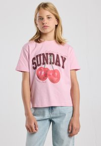 Camiseta de algodón rosa con mangas cortas, que presenta un diseño gráfico de dos cerezas rojas y la palabra "DOMINGO" en letras gruesas.