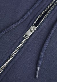 Felpa navy in tessuto con superficie testurizzata, dotata di zip in metallo argentato, cordoncino intrecciato e cuciture rinforzate lungo la zip.