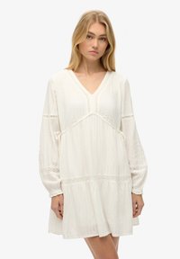 Vestido mini blanco con textura, escote en V, mangas largas tipo globo y detalles de encaje en el dobladillo y las mangas. Se ata en la cintura.