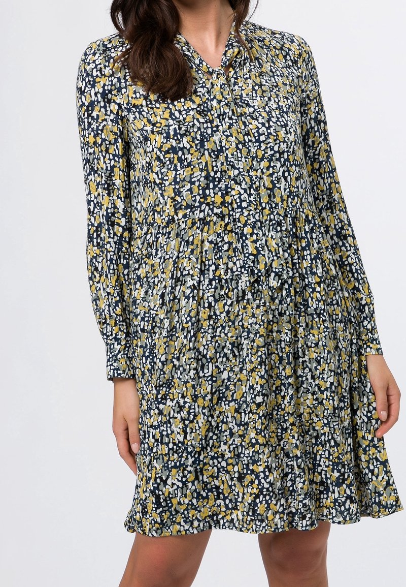 Robe florale marine avec des motifs jaunes et blancs, manches longues, col boutonné et design de jupe à volants. Texture de tissu léger.