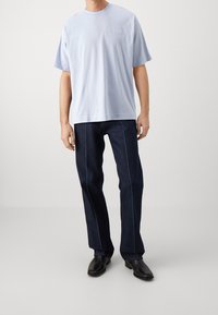 Camiseta de manga corta azul claro combinada con jeans azul oscuro con costuras contrastantes, completada con botas negras hasta el tobillo.