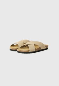 Sandale bej din suede, cu curele încrucișate, talpă din plută și talpă din cauciuc texturat negru, concepute pentru confort și utilizare casuală.