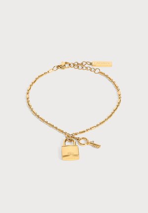 Goldfarbiges Perlenkettenarmband mit Vorhängeschloss- und Schlüssel-Anhängern, Lacoste-Logo am Schloss und rechteckigem Anhänger nahe dem Verschluss.