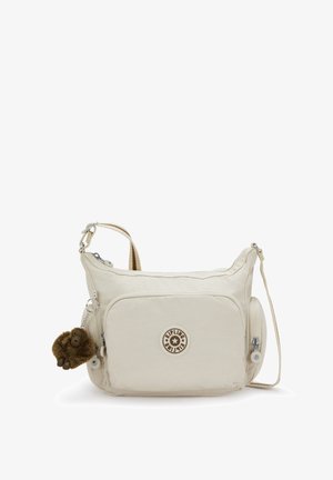 Beige vuorilaukku, joka on valmistettu pehmeästä kankaasta. Siinä on etutasku vetoketjulla, brändilogolla ja karvainen apinanmuotoinen avainkoru.