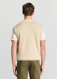Pull sans manches en maille beige avec un col rond, associé à une chemise à manches courtes de couleur claire ; texture lisse et coupe décontractée.