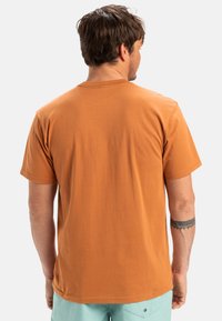 Camiseta de manga corta y cuello redondo en color óxido, hecha de algodón, con una textura suave y sin patrones visibles.