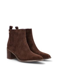 Botas de tobillo de ante marrón con puntera puntiaguda, tacón apilado, lengüetas laterales y una textura suave. Corte bajo alrededor del tobillo.