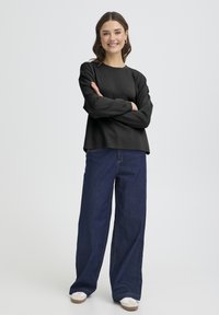 Haut noir à manches longues avec col rond, associé à un jean bleu foncé à jambes larges et des baskets blanches. Texture lisse, coupe décontractée.