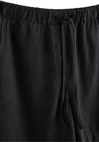 Black loose-fit pants with elastic waistband and fabric drawstring tie at the front center, featuring side seam pockets.