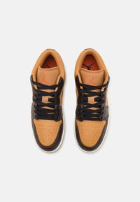 Paire de baskets basses beige et marron foncé avec des lacets noirs et un logo Jumpman rouge sur les languettes, vues de dessus sur un fond blanc.