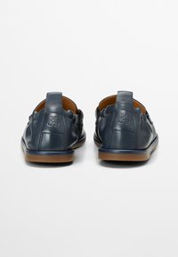 Marine leren schoenen met een gladde afwerking, open achterkant ontwerp en een platte rubberen zool. Kenmerkt ingedrukte initialen "M OP" nabij de hak.