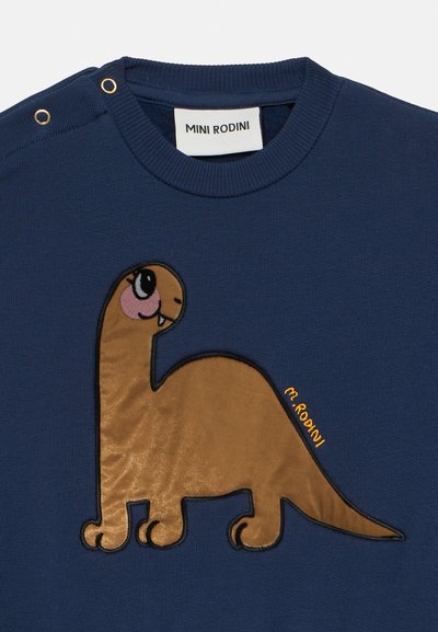 Maglione blu navy con un'applicazione di un dinosauro marrone testurizzato, dettagli rosa sugli occhi e accessori dorati sulla spalla. Etichetta: Mini Rodini.