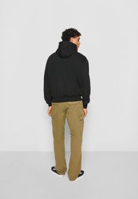 Hoodie noir avec une poche frontale et une capuche à cordon, associé à un pantalon cargo beige clair avec des poches latérales. Baskets noires.