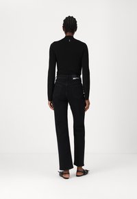 Schwarzes Langarmoberteil mit einem dezenten Logo-Detail auf dem Rücken, kombiniert mit hochgeschnittenen schwarzen Denim-Jeans mit Taschen und geradem Schnitt.