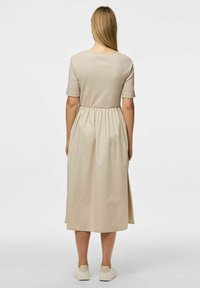 Bež haljina od pamuka s kratkim rukavima, naglašenim strukom i lepršavom suknjom. Ima okrugli izrez i doseže do sredine lista. Bijele tenisice upotpunjuju izgled.