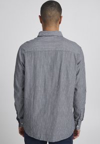 Stripet skjorte med knapper, bakstykke, lange ermer og mansjetter med knapper, laget av lett stoff i nyanser av marineblått og hvitt.