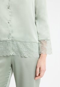 Jasnozielony satynowy komplet piżamowy z wykończeniem koronkowym na dolnej krawędzi i rękawach, zapinany na guziki z przodu, o gładkiej, miękkiej fakturze.
