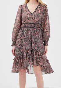 Robe noire et rose à motifs avec des manches longues, décolleté en V, smock au niveau de la taille et ourlet à volants. Tissu léger et transparent avec texture.