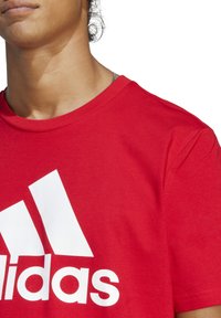 T-shirt in cotone rosso con collo rotondo, caratterizzata da un grande logo Adidas bianco sul petto. Tessuto liscio con maniche corte.
