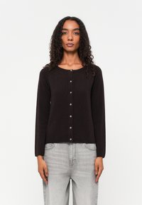 Cardigã preto de mangas longas com decote arredondado, fecho de botões, textura suave e design ajustado, combinado com jeans cinza claro.