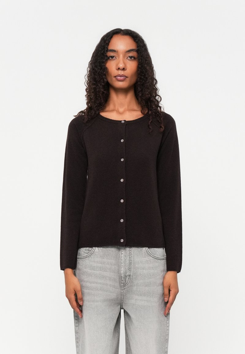 Cardigã preto de mangas longas com decote arredondado, fecho de botões, textura suave e design ajustado, combinado com jeans cinza claro.