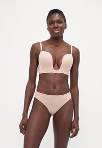 Lett polstret, nudefarget bh med dyp utringning og justerbare stropper; paret med matchende bikinitruser med sløyfe.
