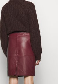 Dunkelbrauner Strickpullover mit übergroßen Ärmeln, kombiniert mit einem eng anliegenden bordeauxroten Lederminirock mit einem Schlitz auf der Rückseite.