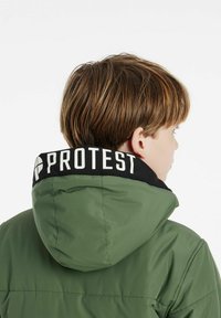Giacca a vento verde con cappuccio, dotata di un colletto nero con la scritta "PROTEST." Texture liscia e design trapuntato sul retro.