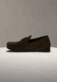 Σκούρο καφέ δερμάτινο παπούτσι τύπου loafer με χαμηλό τακούνι, εμφανίζεται σε ουδέτερη επιφάνεια και φόντο.