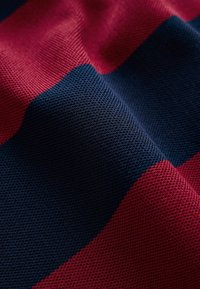 Gros plan sur un tissu texturé avec des rayures horizontales alternées en bleu foncé et rouge profond.
