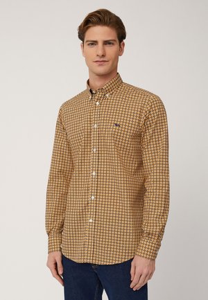 Camicia a maniche lunghe con bottone di colore giallo, caratterizzata da un motivo geometrico con accenti blu e bianchi. Tessuto morbido, colletto classico, design aderente.