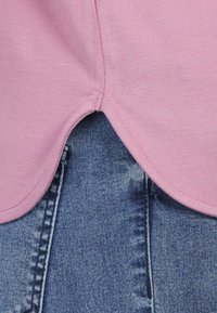 Hellrosa Kurzarmhemd mit abgerundetem Saum überlappt blaue Jeans aus Denim, die eine ausgewaschene Textur und sichtbare Nähte aufweisen.