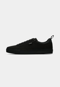 Sneaker nera in tela con punta rotonda, suola piatta e design con lacci. Presenta una linguetta posteriore e un logo discreto sul lato.