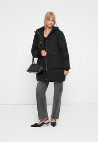 Svart polstret jakke med hette, trykknapplukking og to frontlommer. Kombinert med høyhorror grå jeans og svarte slingback-sko.