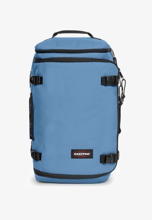 Lyseblå Eastpak-rygsæk med sorte lynlåse, sidelomme i net, kompressionsstropper og et top-håndtag, vist forfra.
