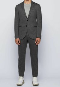 Szary garnitur z dopasowaną marynarką i slim-fit spodniami, w połączeniu z jasnoszarym podkoszulkiem i białymi sneakersami. Gładka faktura i minimalistyczny design.