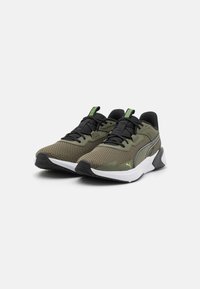 Baskets de sport en maille verte avec des accents noirs, tige texturée, semelle blanche contrastante et détails réfléchissants sur le côté et la languette.