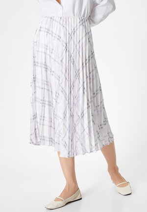 Falda plisada de tela blanca translúcida con un patrón de cuadros en púrpura y gris. Cintura elástica y corte hasta los tobillos. Combinada con bailarinas beige.