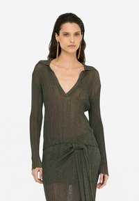 Langärmliger Strickpullover in Dunkelgrün mit V-Ausschnitt, geripptem Muster und gewelltem Saum. Verfügt über einen Kragen und eine taillierte Silhouette.