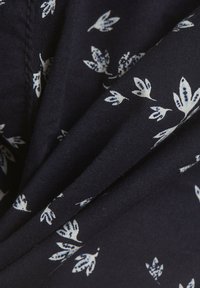 Námořnická tkanina s jemným bílým květinovým vzorem. Textilie má měkkou strukturu s výraznými záhyby, což zdůrazňuje její schopnost rovnání.