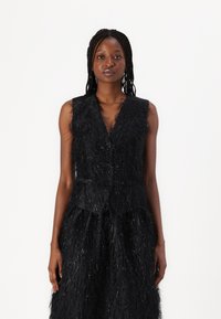 Black vest with textured fringe detail, sleeveless design, v-neck, and front button closure. Accented with shiny strands throughout.