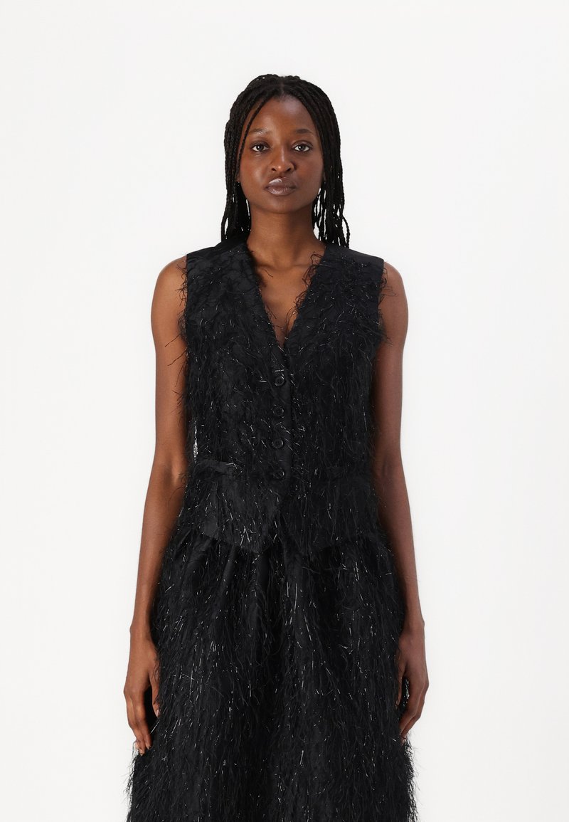 Black vest with textured fringe detail, sleeveless design, v-neck, and front button closure. Accented with shiny strands throughout.