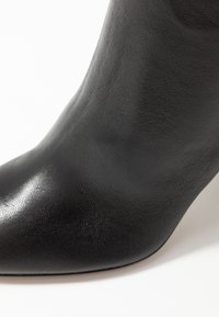 Černá kožená kotníková bota s špičatou špicí, hladkým povrchem a elegantním designem. Obsahuje jemné švy podél okrajů.
