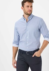 Hellblaues Hemd mit Knopfleiste und kleinem Muster, hochgekrempelte Ärmel, kombiniert mit dunkler Hose und strukturiertem marineblauem Gürtel.