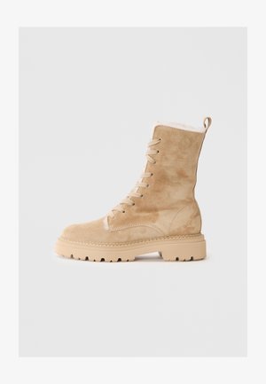 Bottes en daim beige à mi-mollet avec lacets, doublure en peluche, semelle en caoutchouc antidérapante et détails de couture le long de la semelle pour un aspect texture supplémentaire.