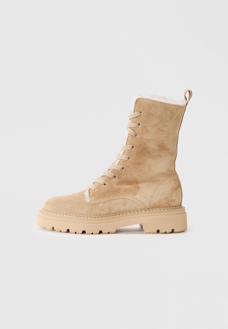 Bottes en daim beige à mi-mollet avec lacets, doublure en peluche, semelle en caoutchouc antidérapante et détails de couture le long de la semelle pour un aspect texture supplémentaire.