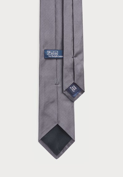 Satricis tumši pelēks tauriņš ar baltu rakstu, kurā ir zila birka ar uzrakstu "Polo by Ralph Lauren" un etiķete, kas norāda "Roku darbs Itālijā".